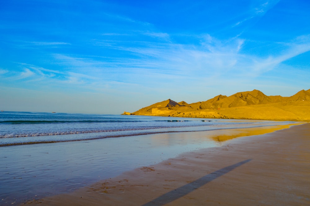 a sandy beach next to the ocean under a blue sky