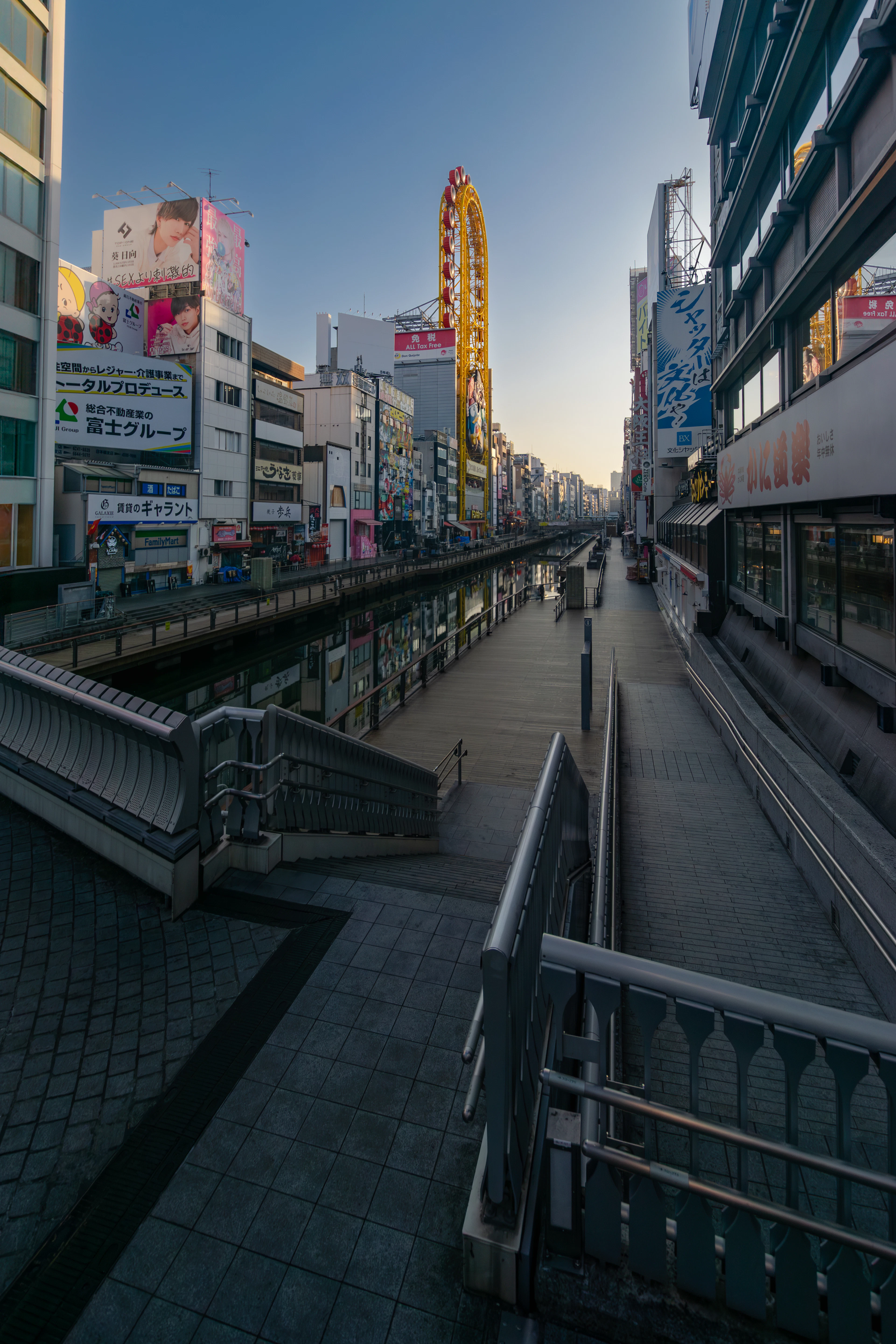 Empty boardwalks line the Dotonbori canal at dawn, with a Ferris wheel visible in the distance.