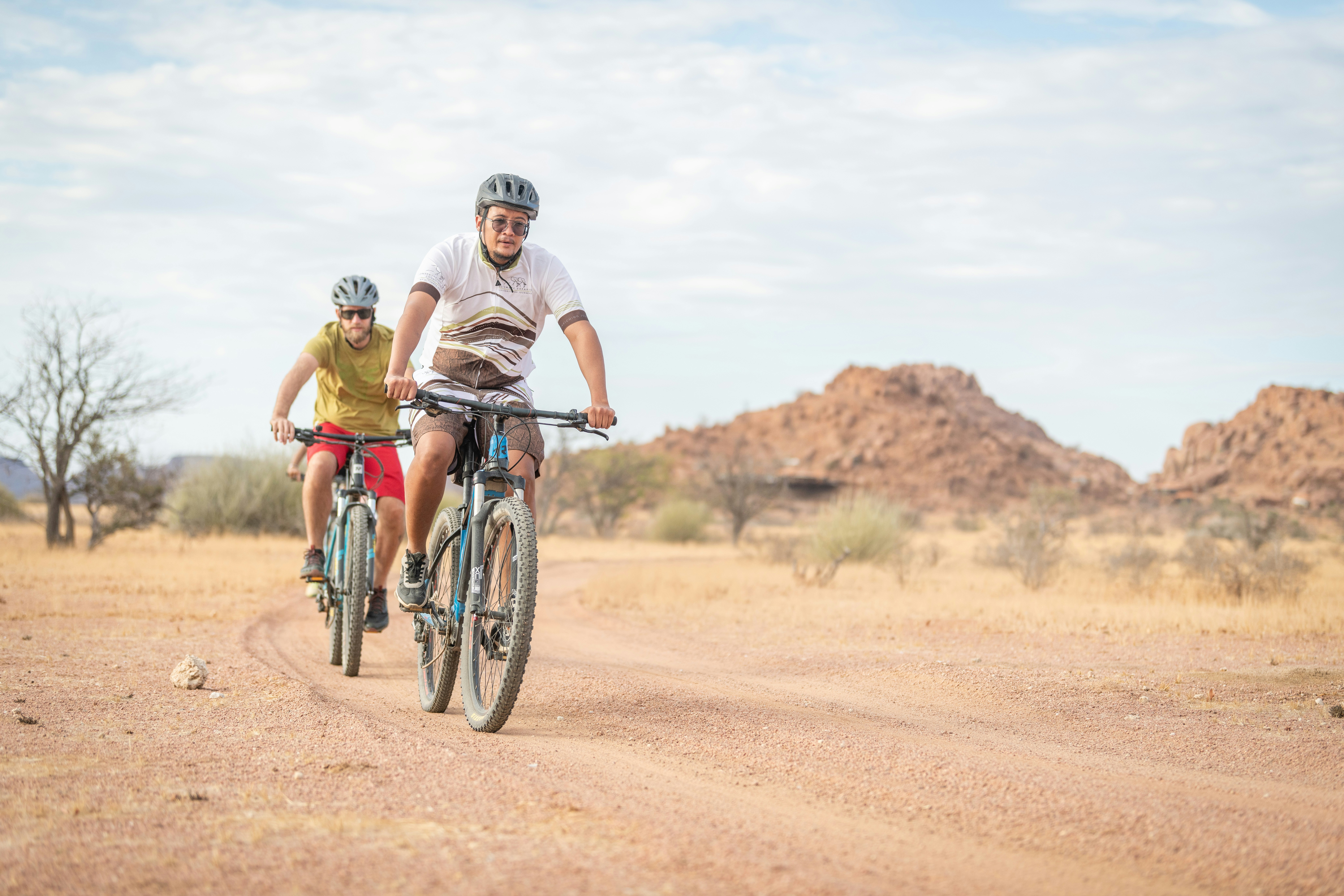 a couple of people riding bikes down a dirt road