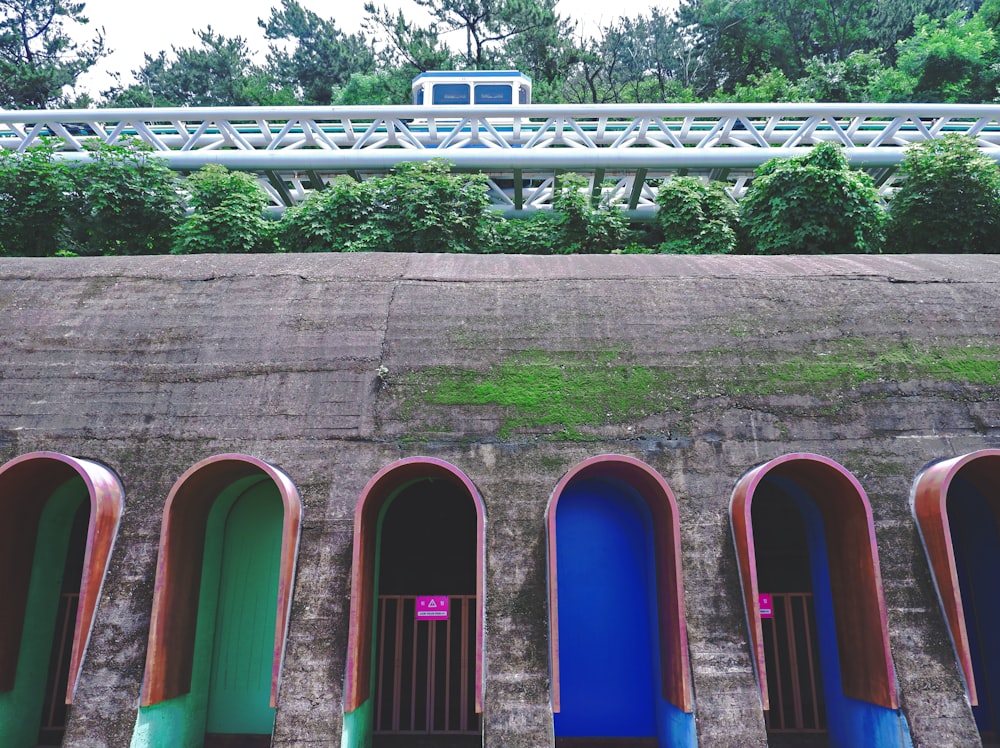 a row of blue, green, and red toilets next to a bridge