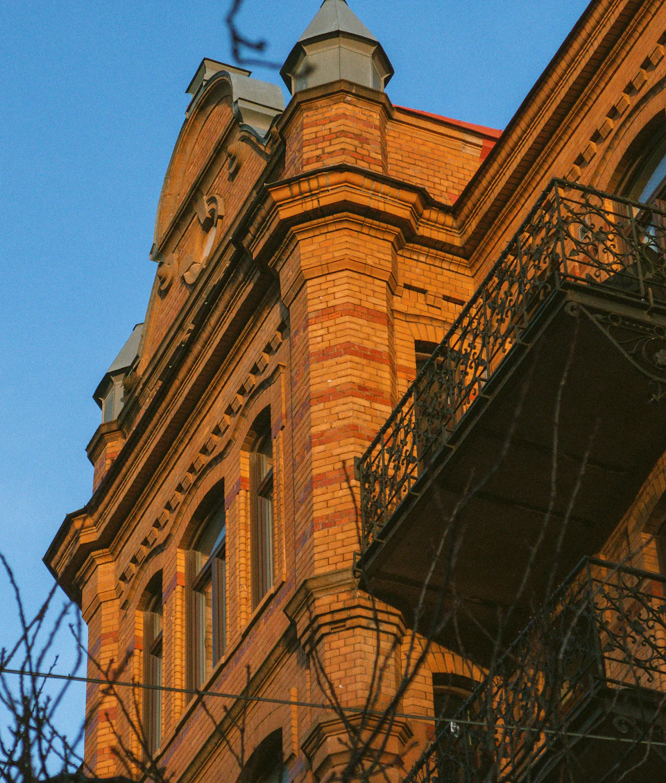 Tall ornate brick building with pointed roof and dome stands prominently above trees
