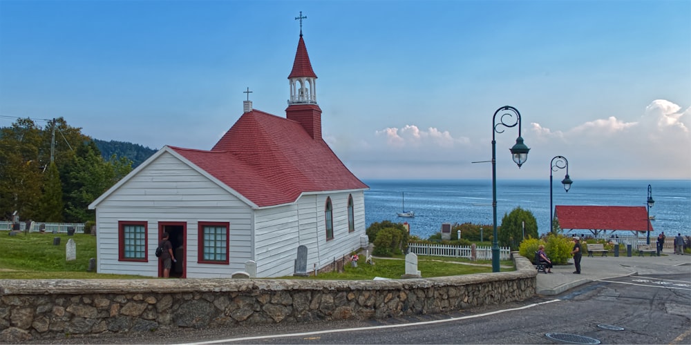 a white church with a red roof next to the ocean