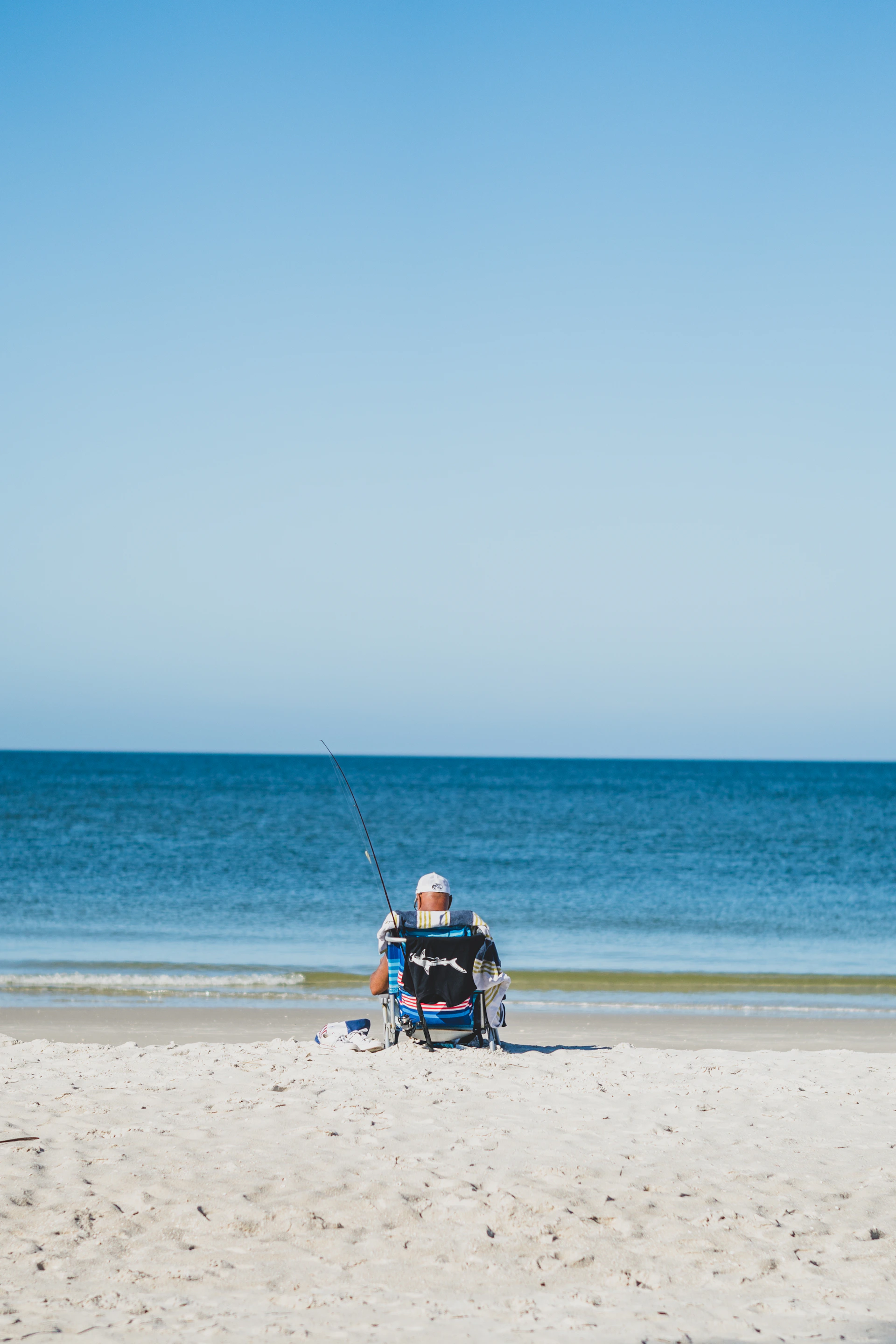 a man sitting in a chair fishing on the beach