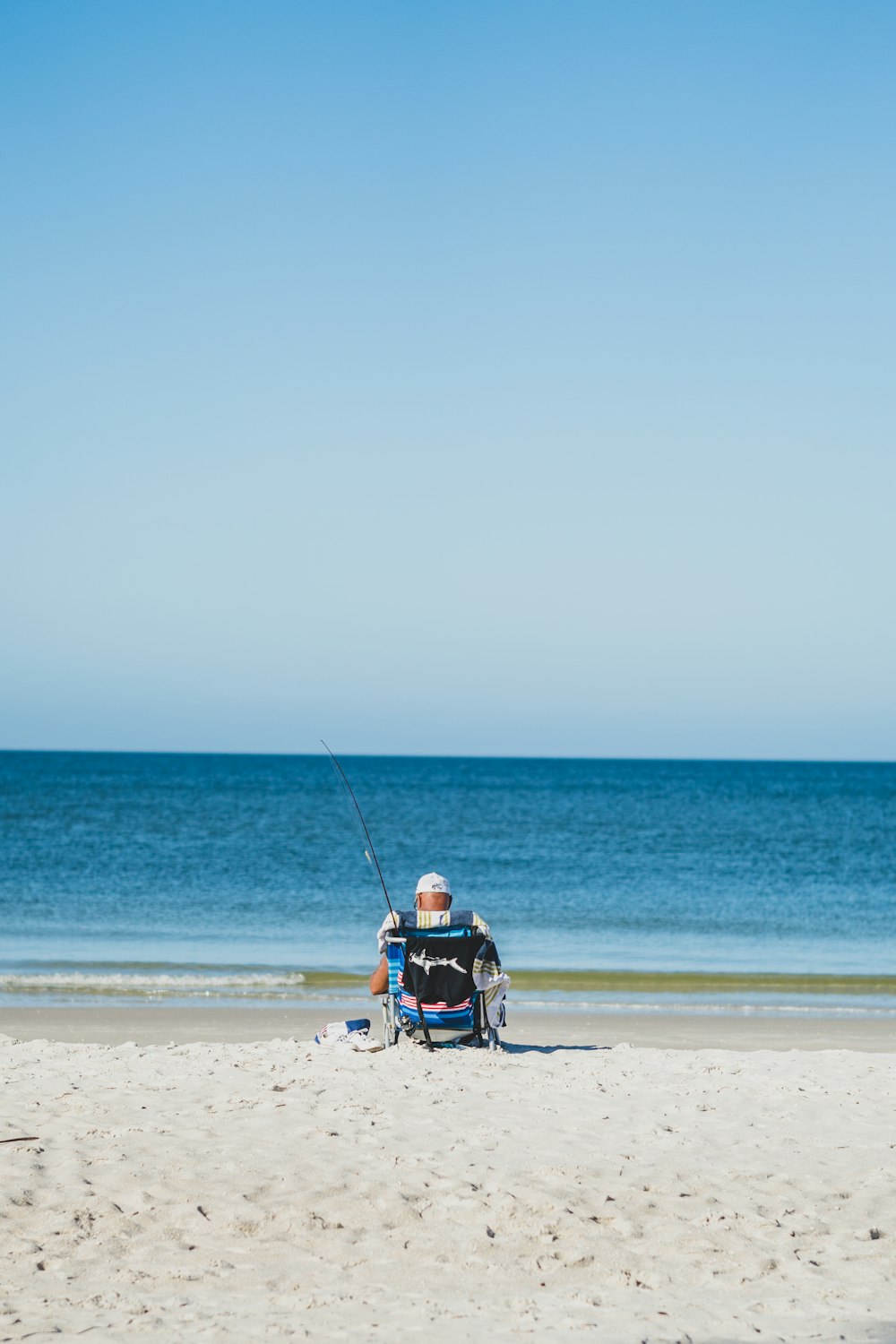 a man sitting in a chair fishing on the beach