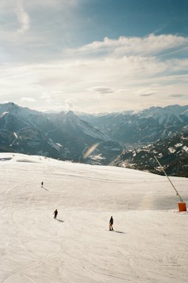 A wide snowy piste with a lone skier and a lift cable at Serre Chevalier, looking down the valley toward Briançon