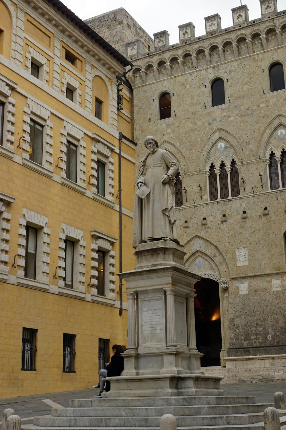 una persona seduta su una statua di pietra di fronte a un edificio