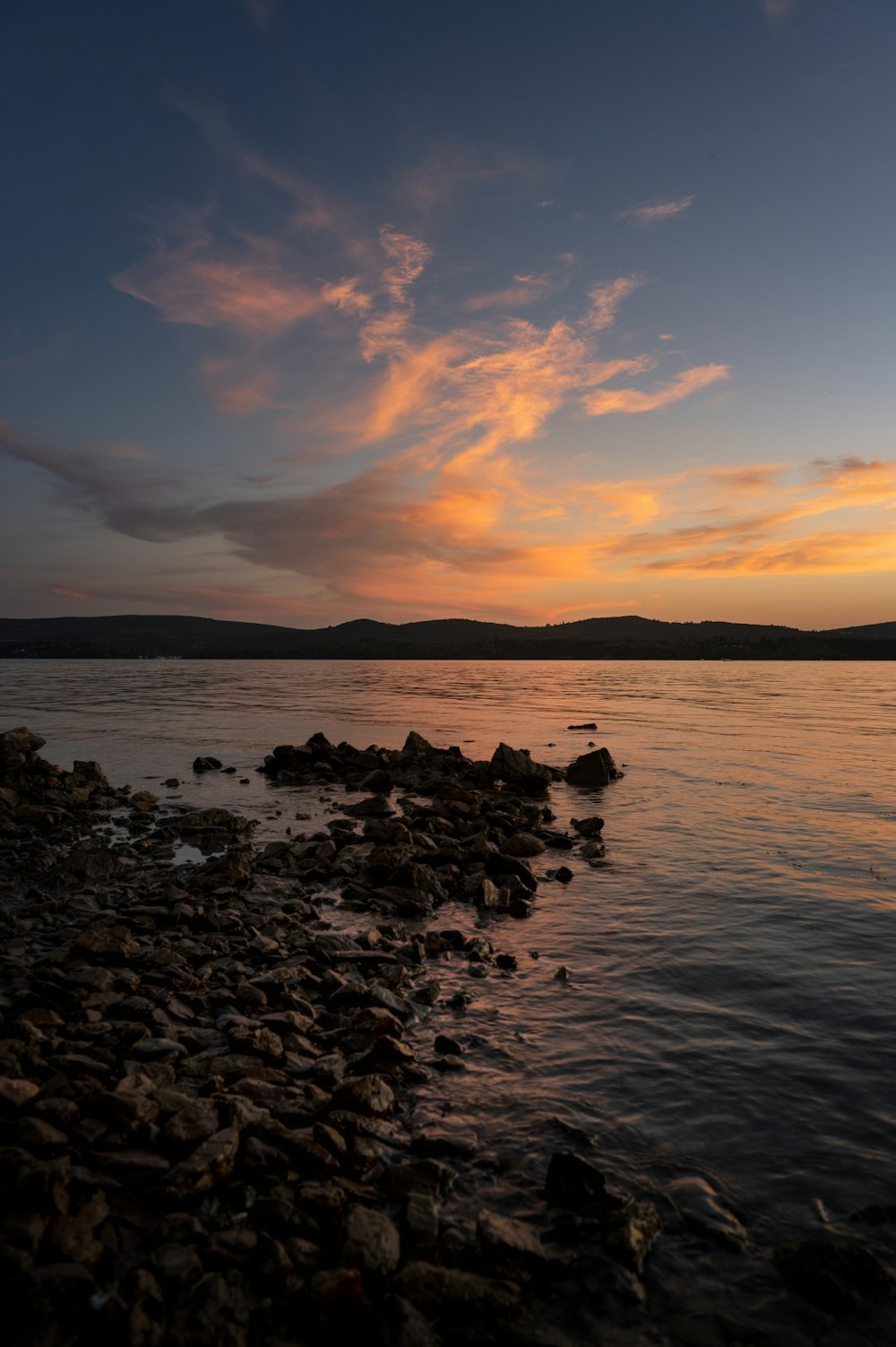 the sun is setting over the water and rocks