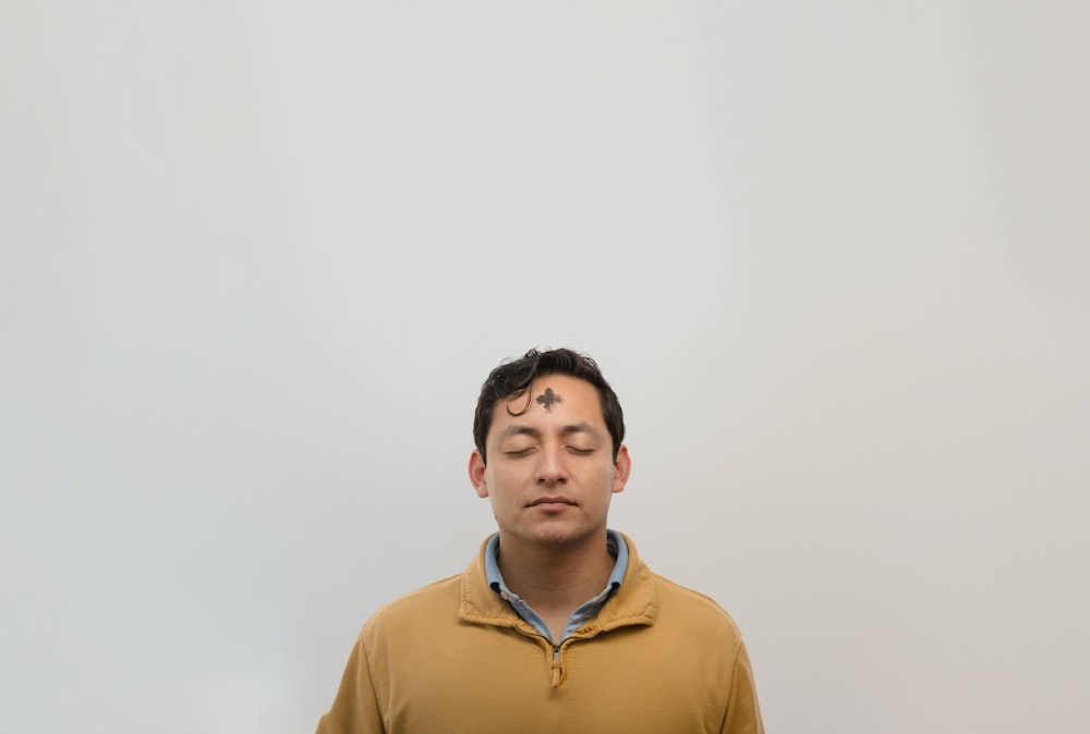 a man with his eyes closed standing in front of a white wall