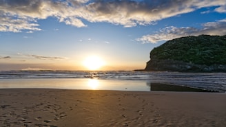 the sun is setting on the beach with footprints in the sand