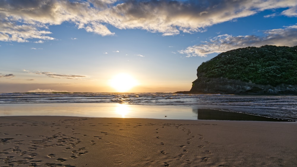 the sun is setting on the beach with footprints in the sand