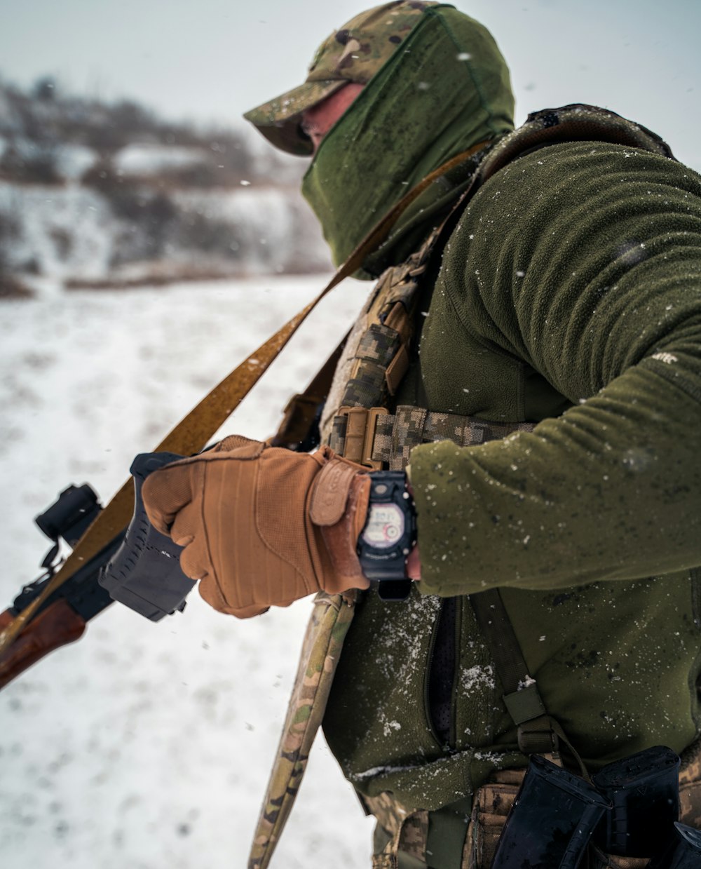a man in a green jacket holding a gun in the snow