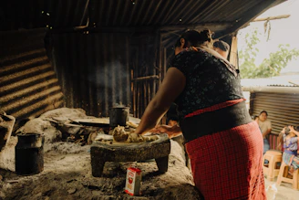 a woman cooking food on a stove in a hut