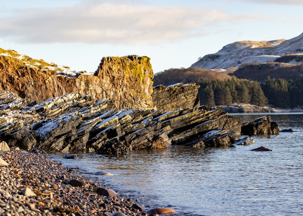 a rocky shore with a body of water and mountains in the background