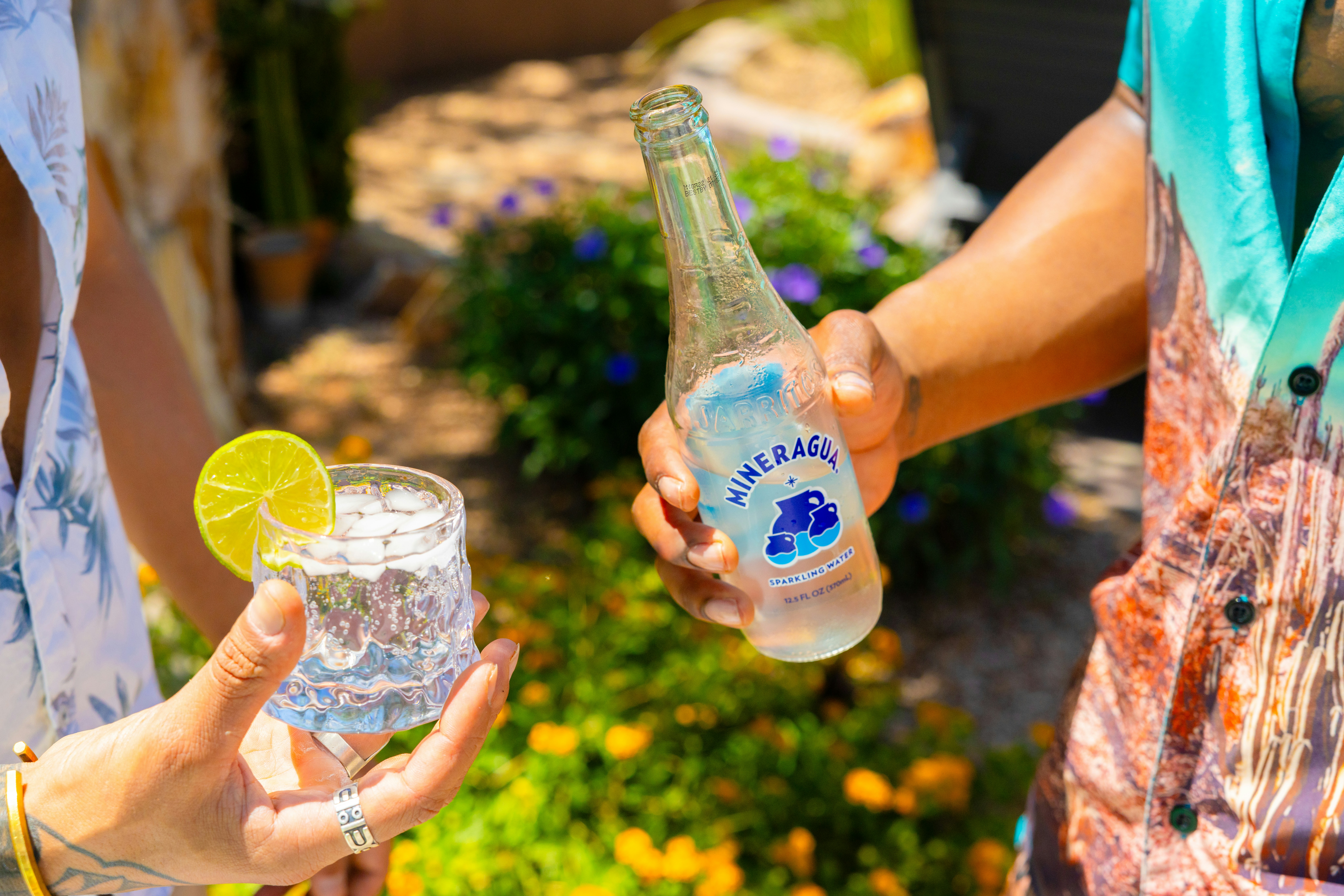Hands hold sparkling water drinks outdoors on a sunny day.