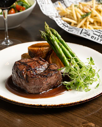 a plate of steak and asparagus with a glass of wine