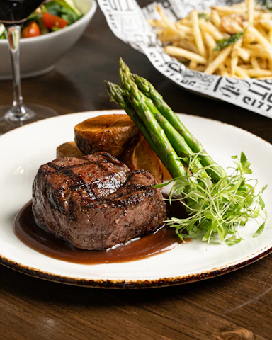 a plate of steak and asparagus with a glass of wine