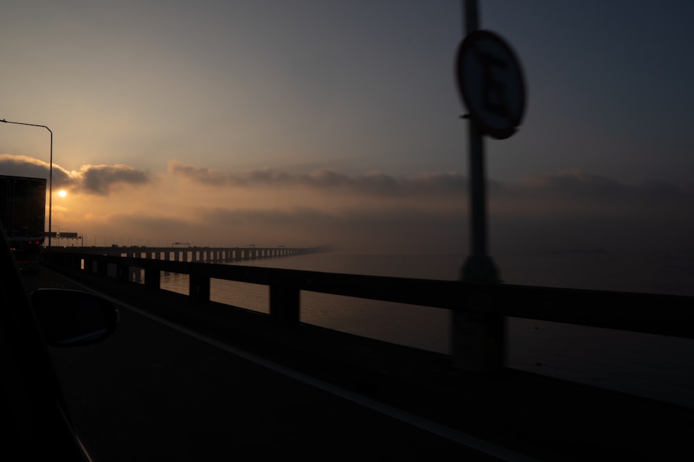 the sun is setting over the water from a bridge