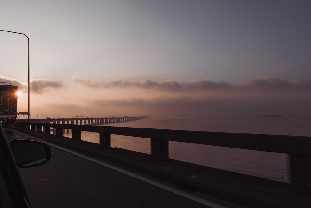 the sun is setting over the ocean and a bridge