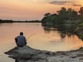 a man sitting on top of a rock next to a river