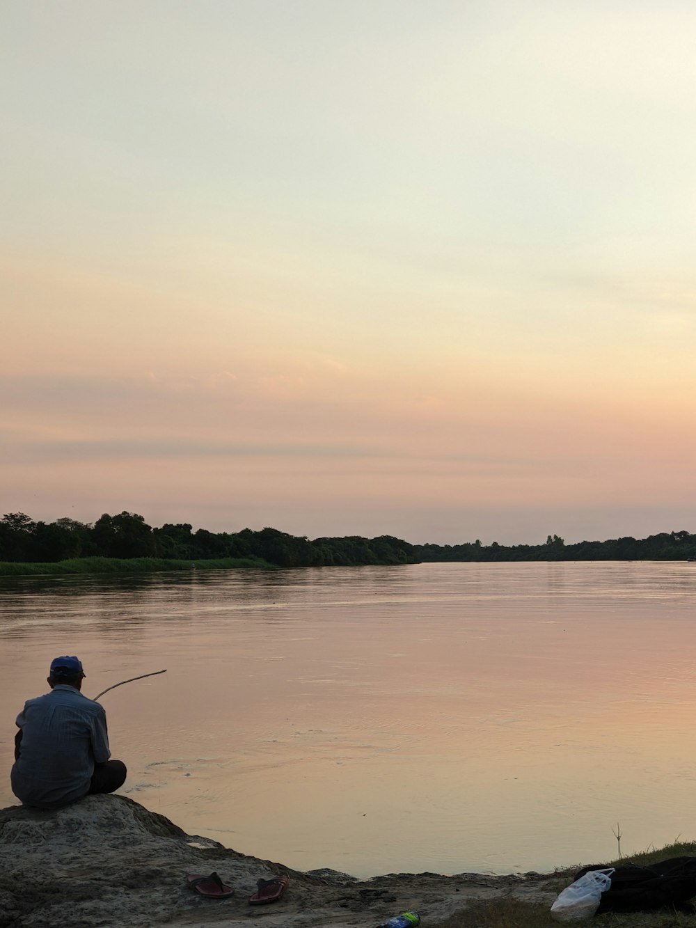 a man sitting on a rock next to a body of water