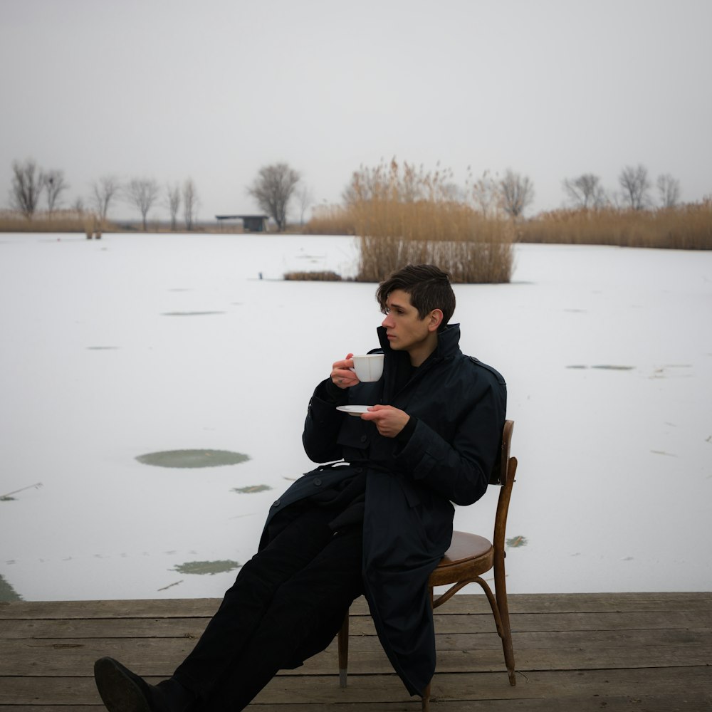 a man sitting on a wooden deck drinking a cup of coffee