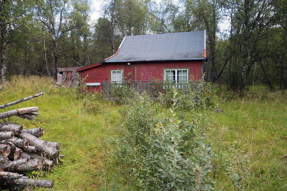 a red house in the woods with a pile of logs in front of it