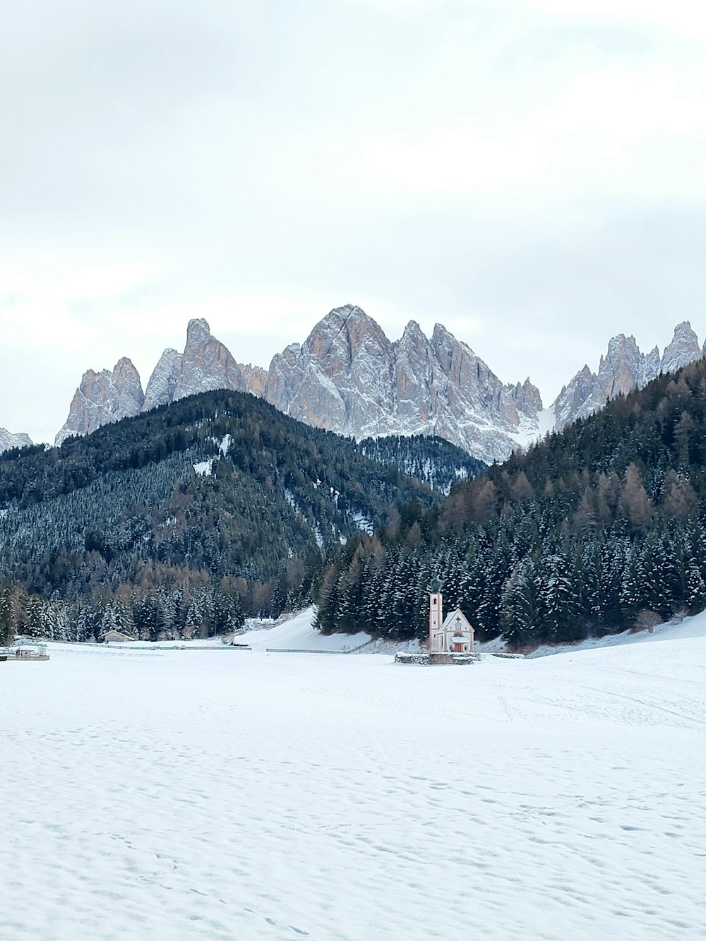 eine verschneite Landschaft mit einer Kirche und Bergen im Hintergrund