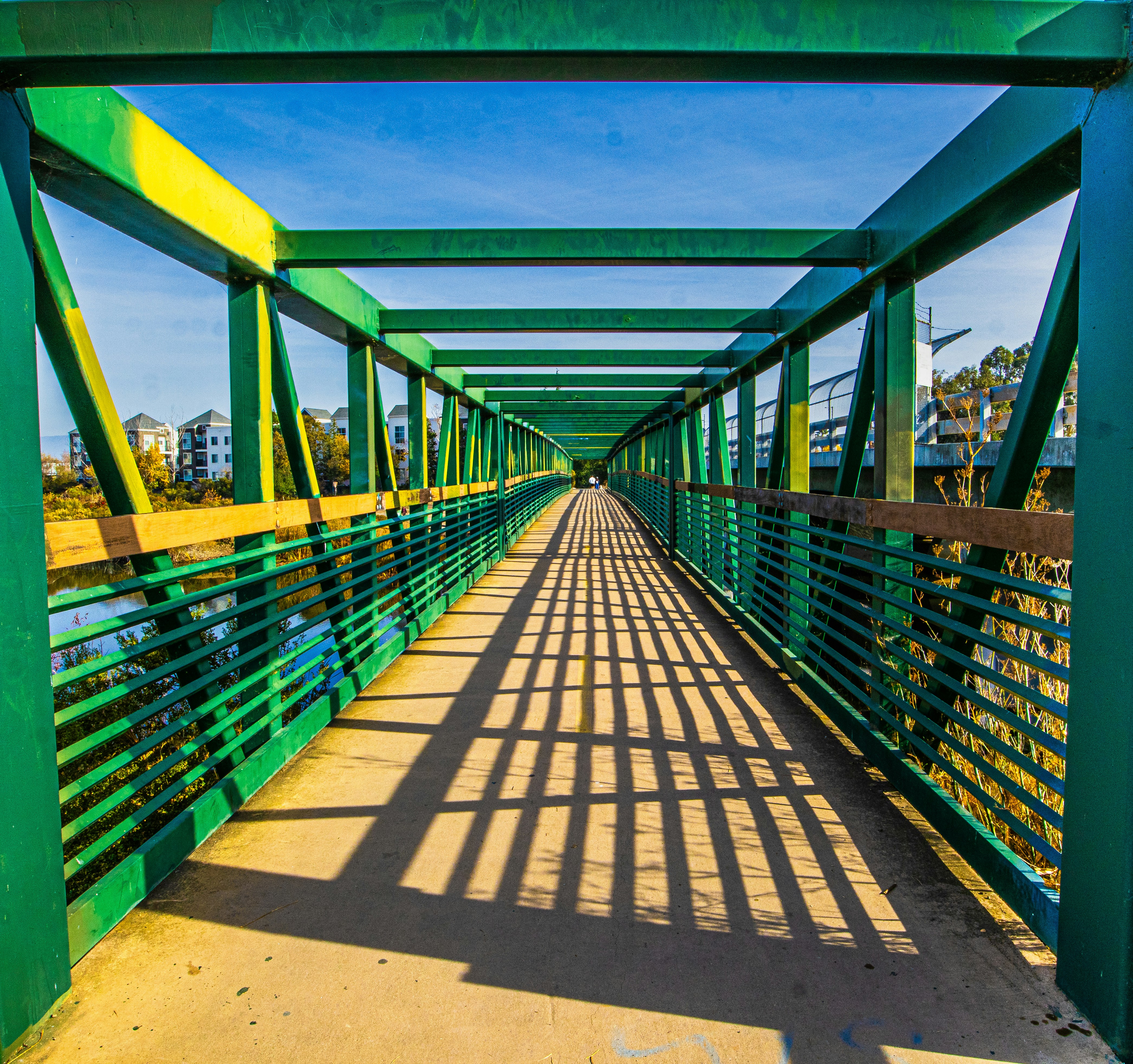 a green bridge with a long shadow on the ground