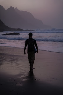 a man walking on the beach at sunset