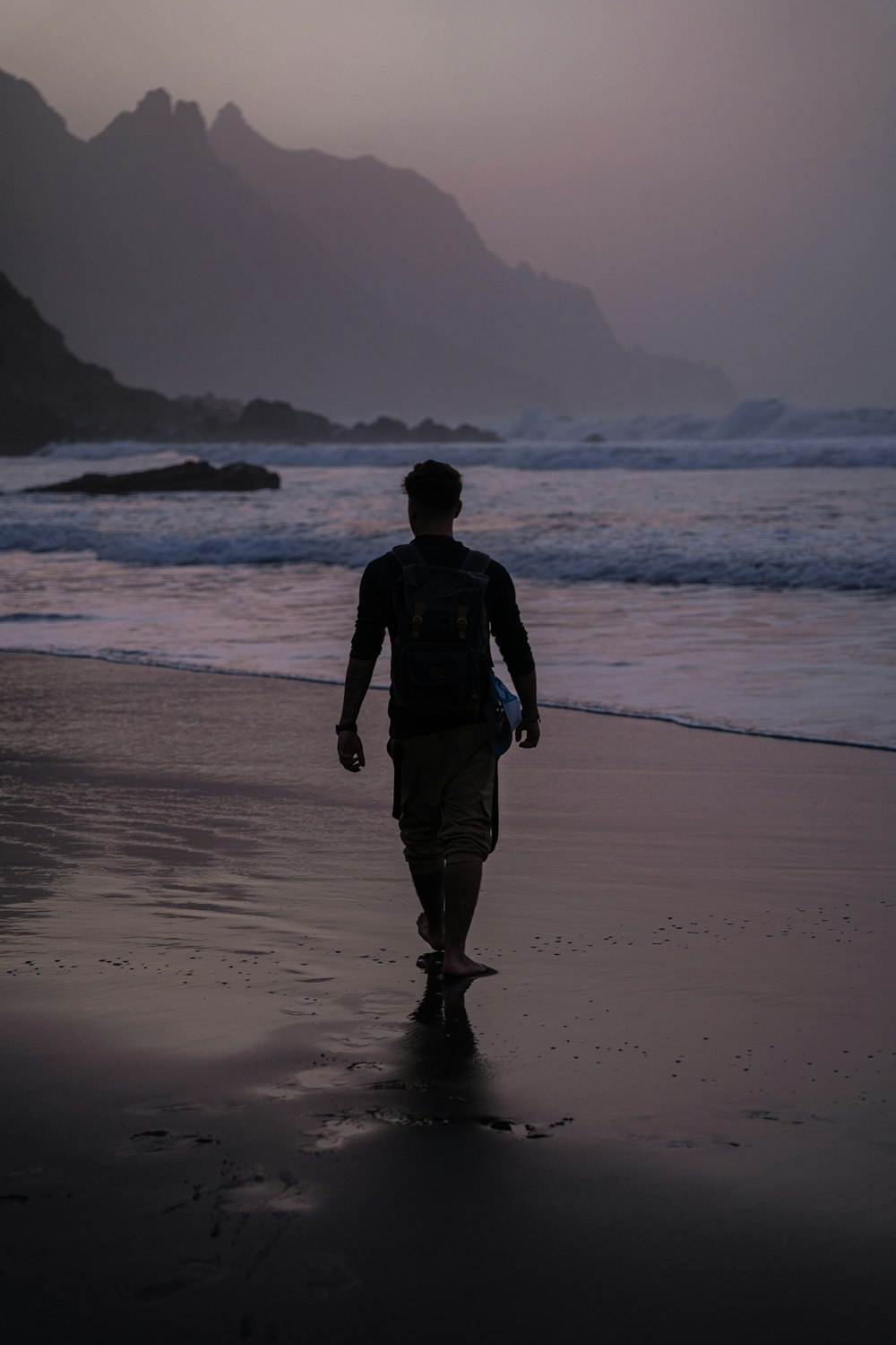 a man walking on the beach at sunset