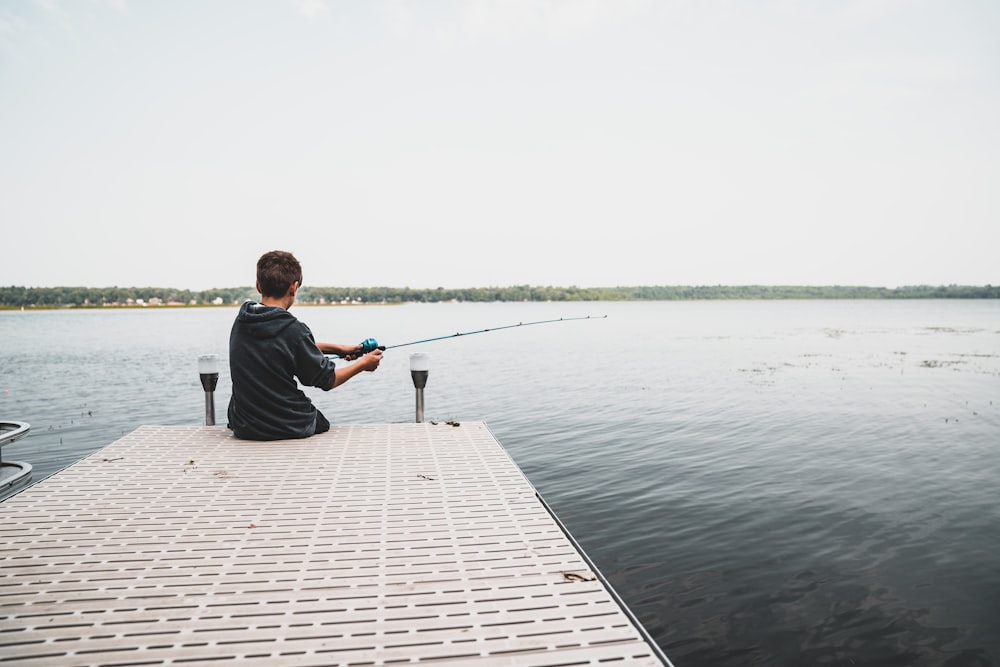 a man sitting on a dock fishing on a lake