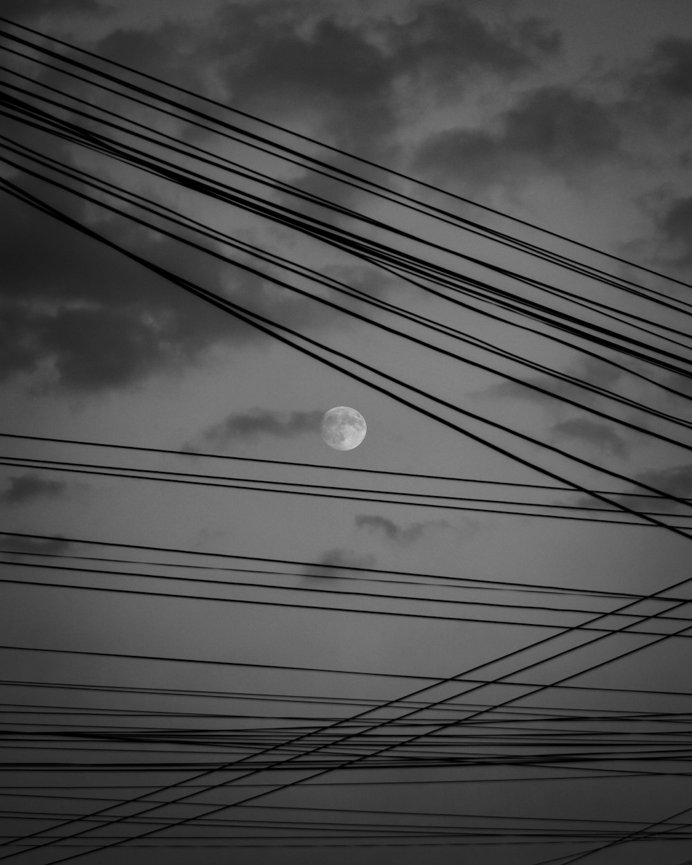 a full moon is seen through power lines