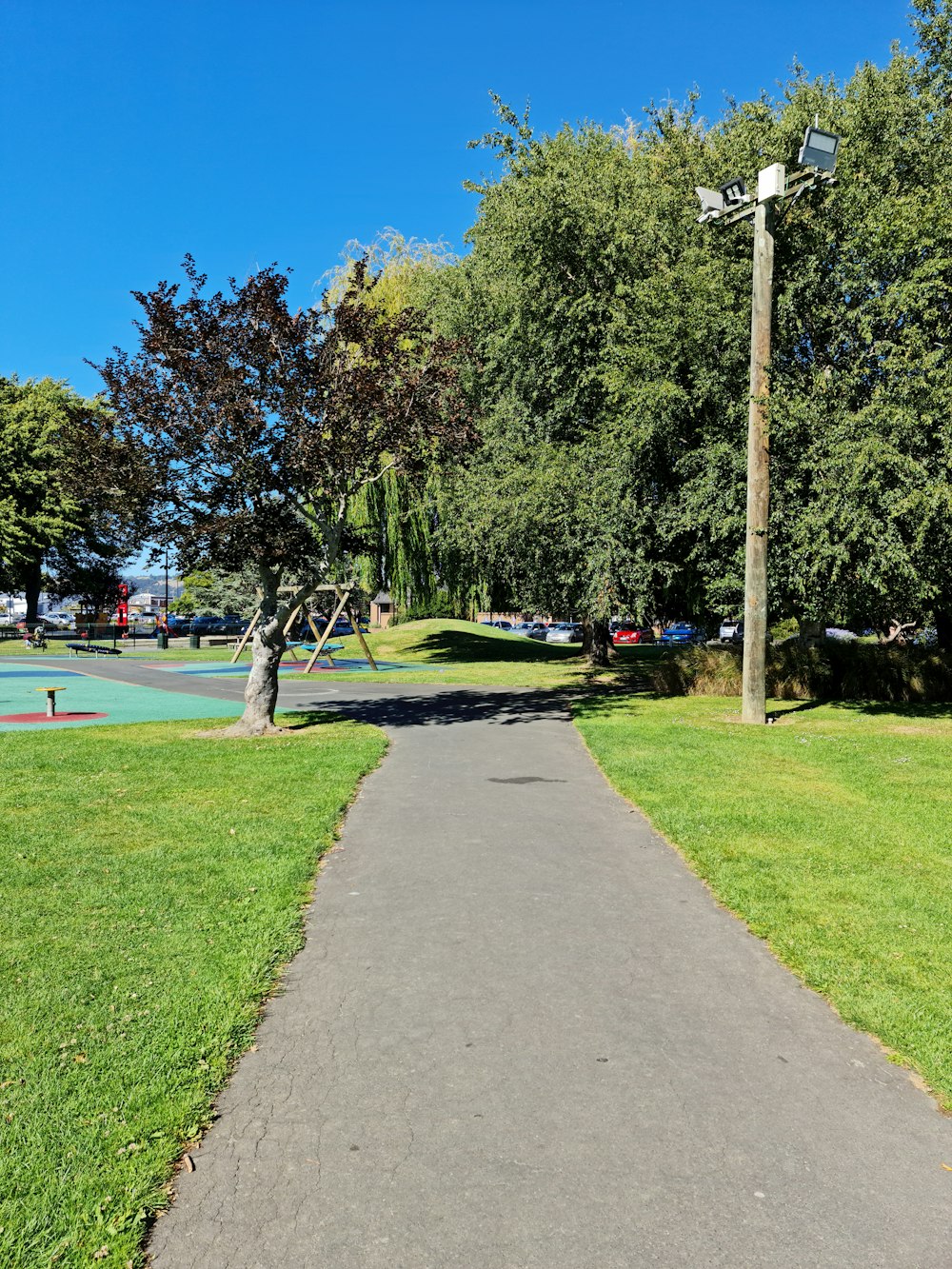 a paved path in a park with a playground in the background