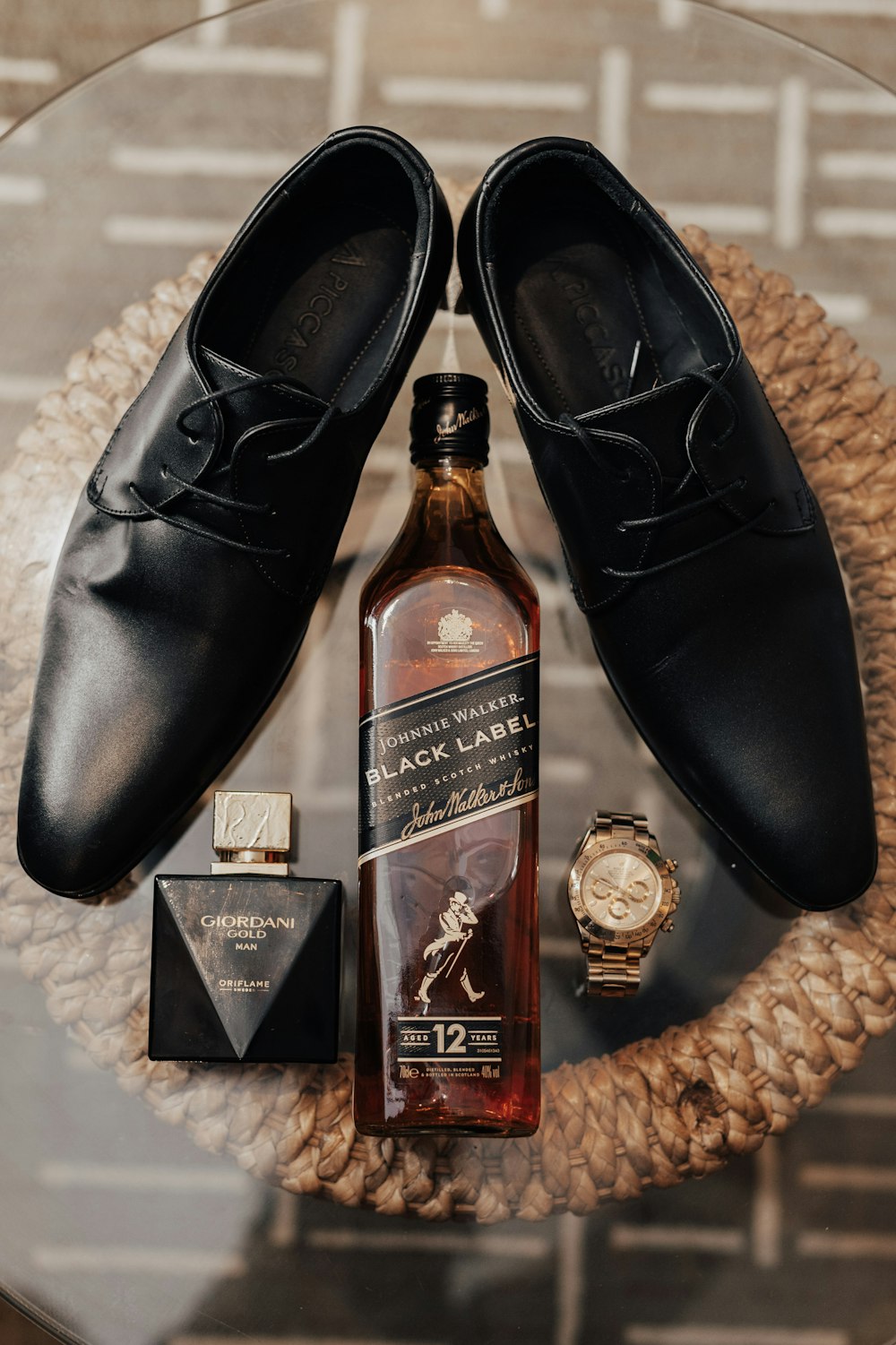 a bottle of whisky, a watch, and a pair of shoes on a table
