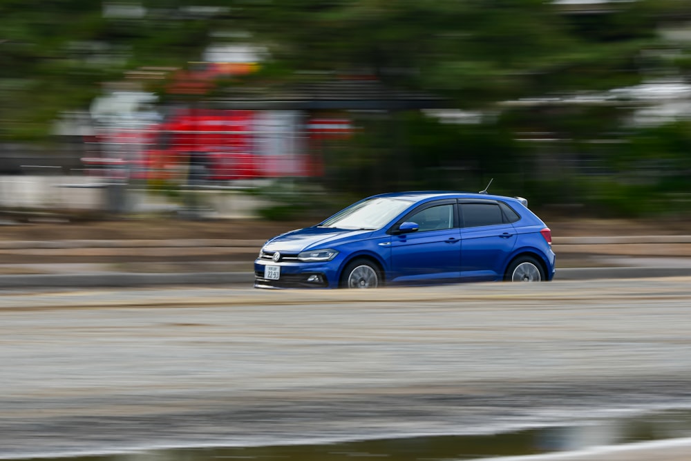 a blue car driving down a street next to a forest