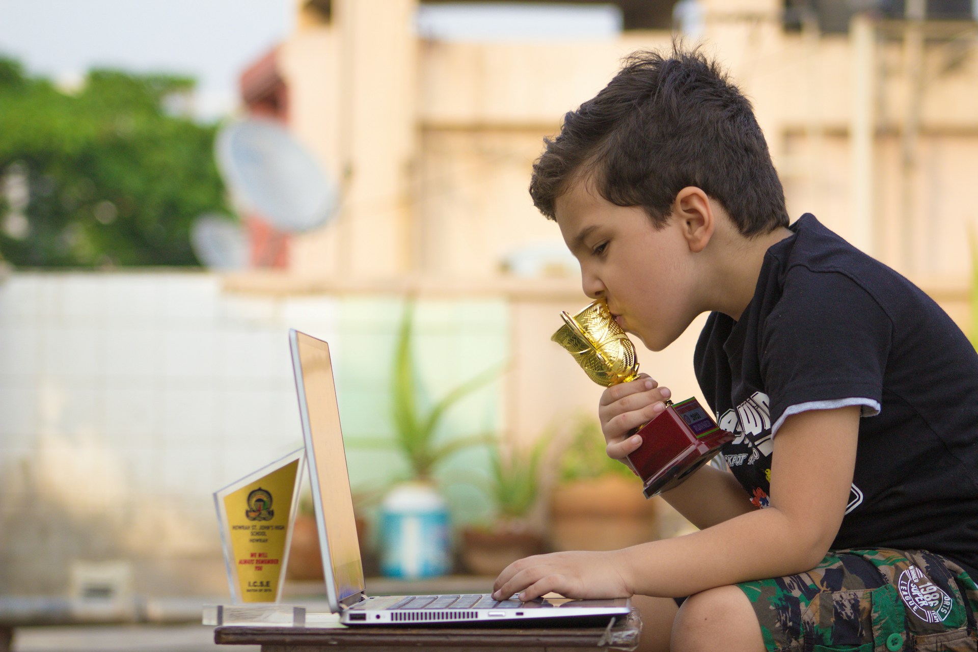 a young boy drinking from a cup while using a laptop