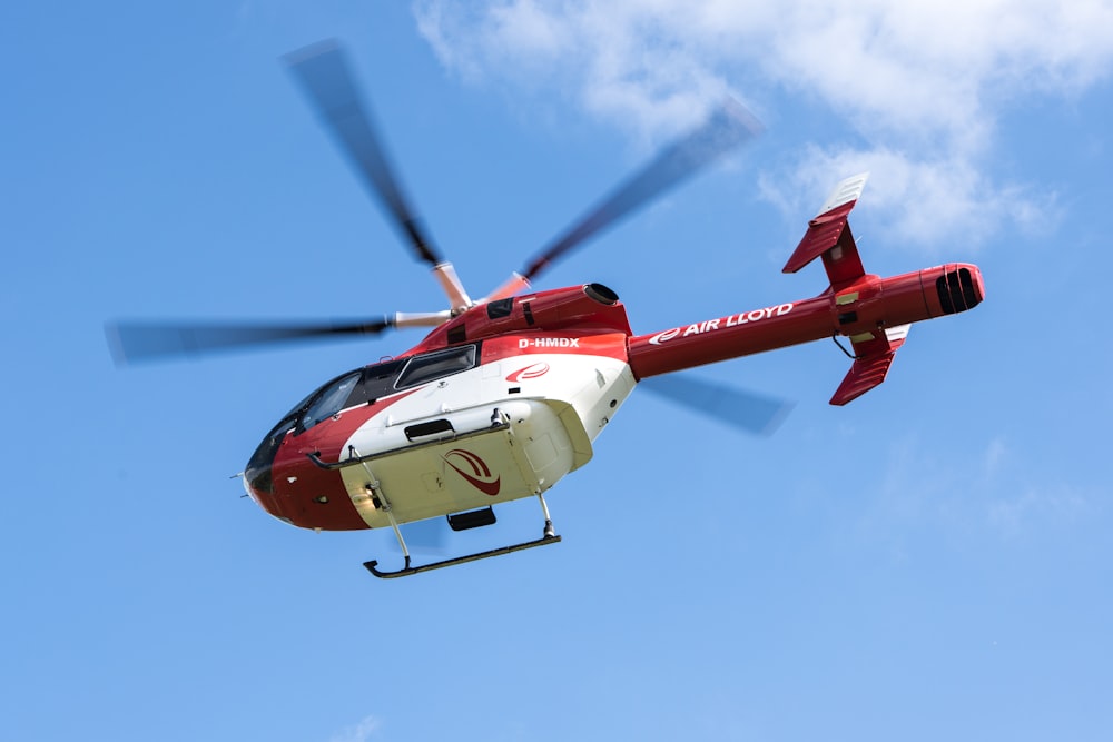 a red and white helicopter flying through a blue sky