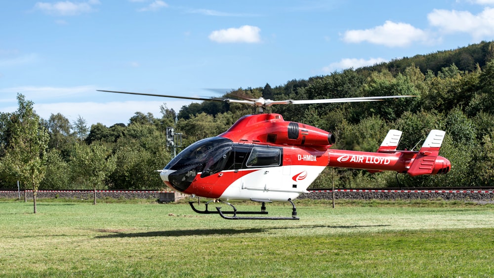 a red and white helicopter sitting on top of a lush green field