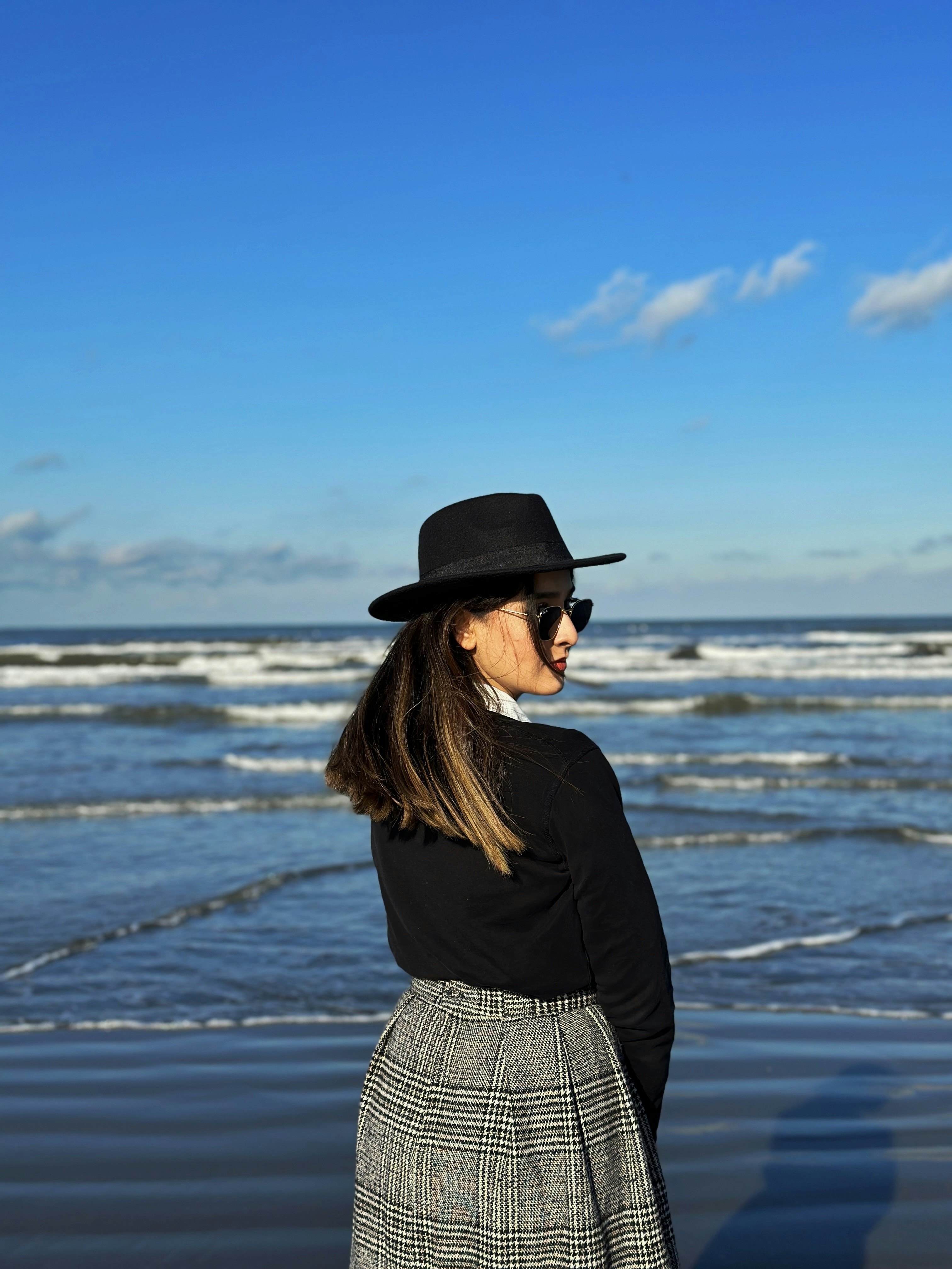 a woman standing on a beach wearing a black hat