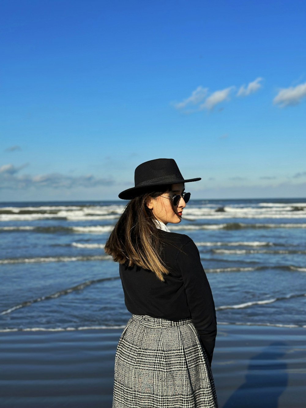 a woman standing on a beach wearing a black hat