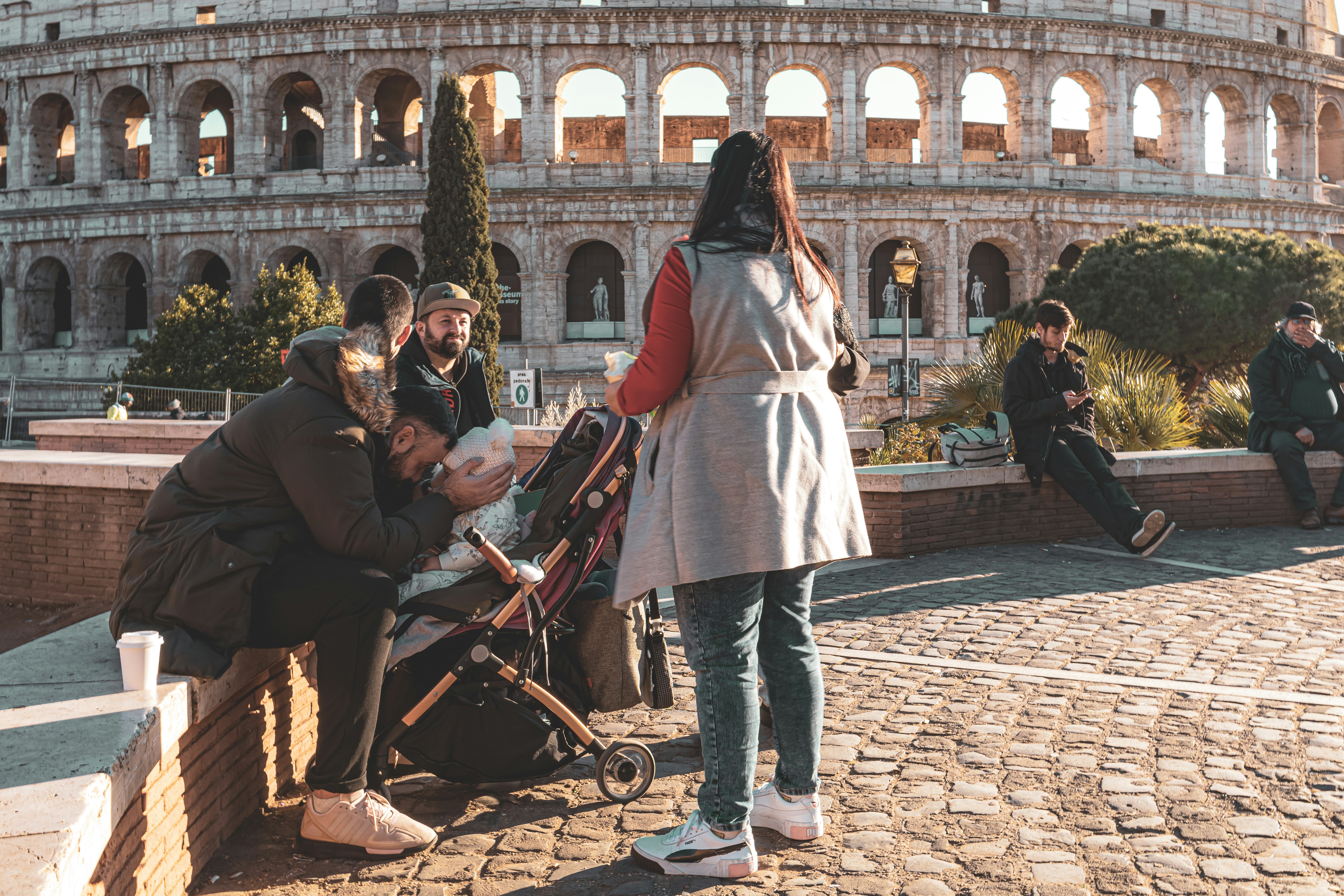Family pausing with a stroller on a cobbled square in front of the Colosseum in Rome