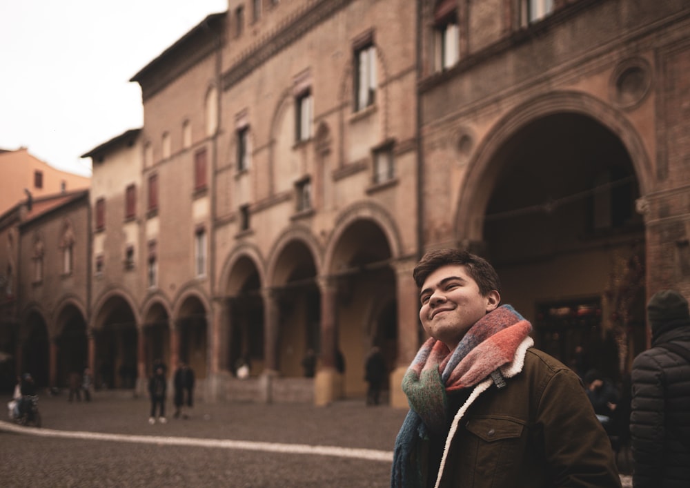 a man standing in front of a building with a scarf around his neck