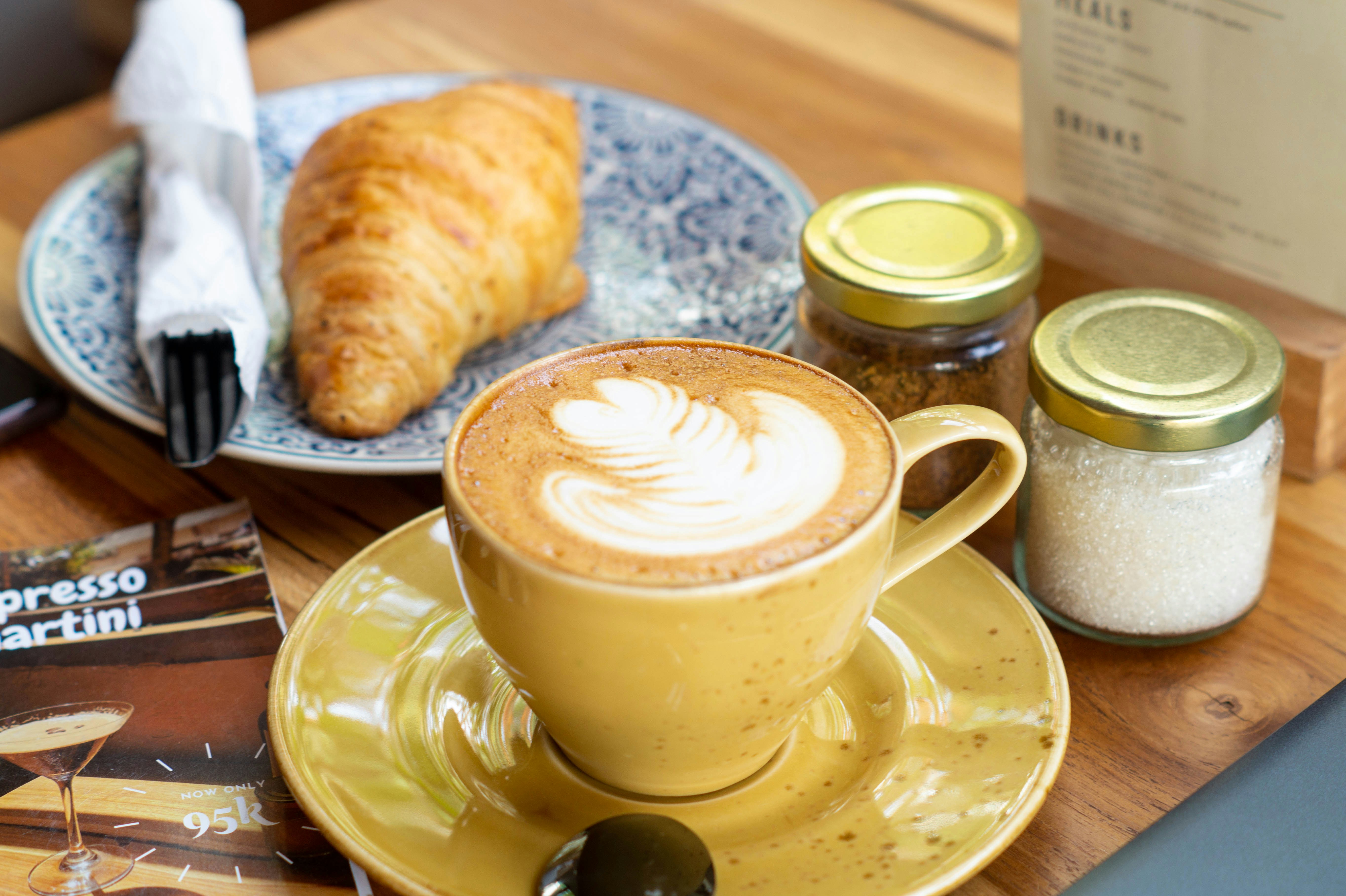 a cup of cappuccino on a plate with a croissant and