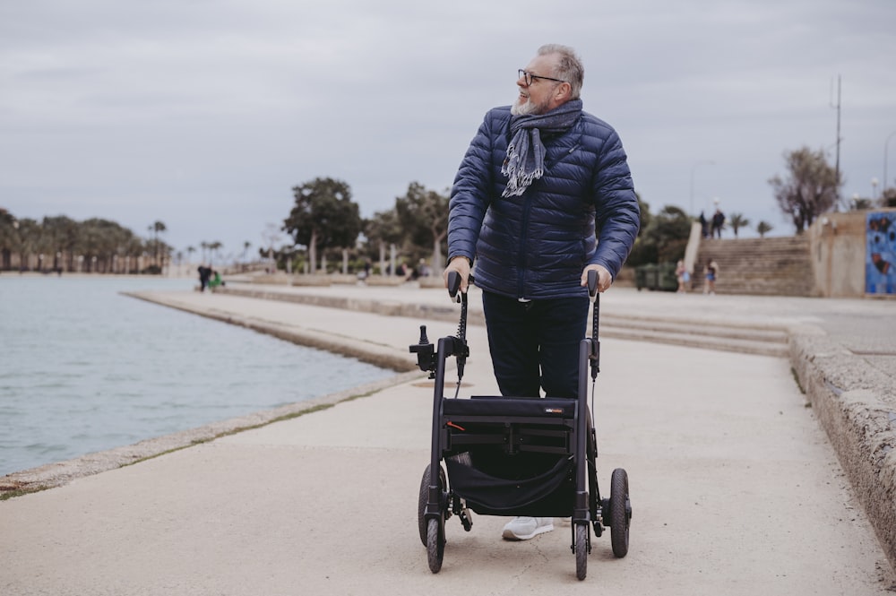 an older man pushing a stroller next to a body of water