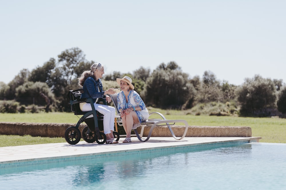 Dos mujeres sentadas en un banco junto a una piscina