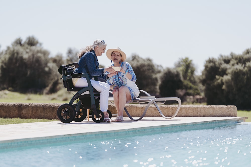 a woman sitting next to a man in a wheel chair near a pool