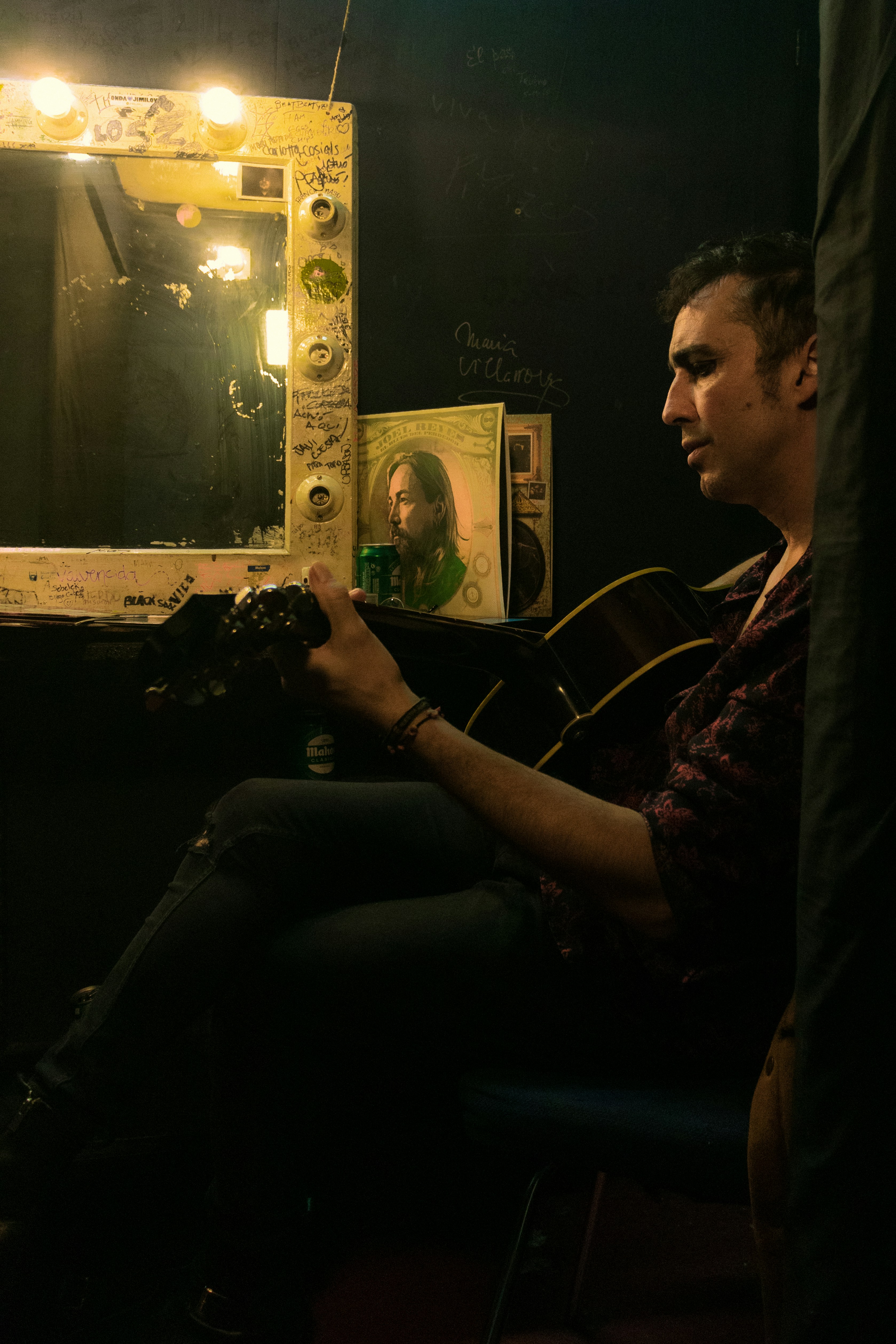 um homem sentado em frente a um espelho segurando uma guitarra