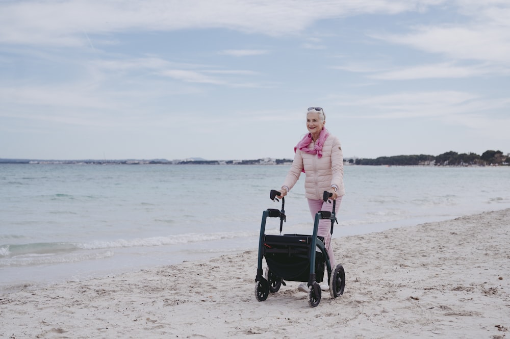 a woman in a pink coat pushing a stroller on the beach