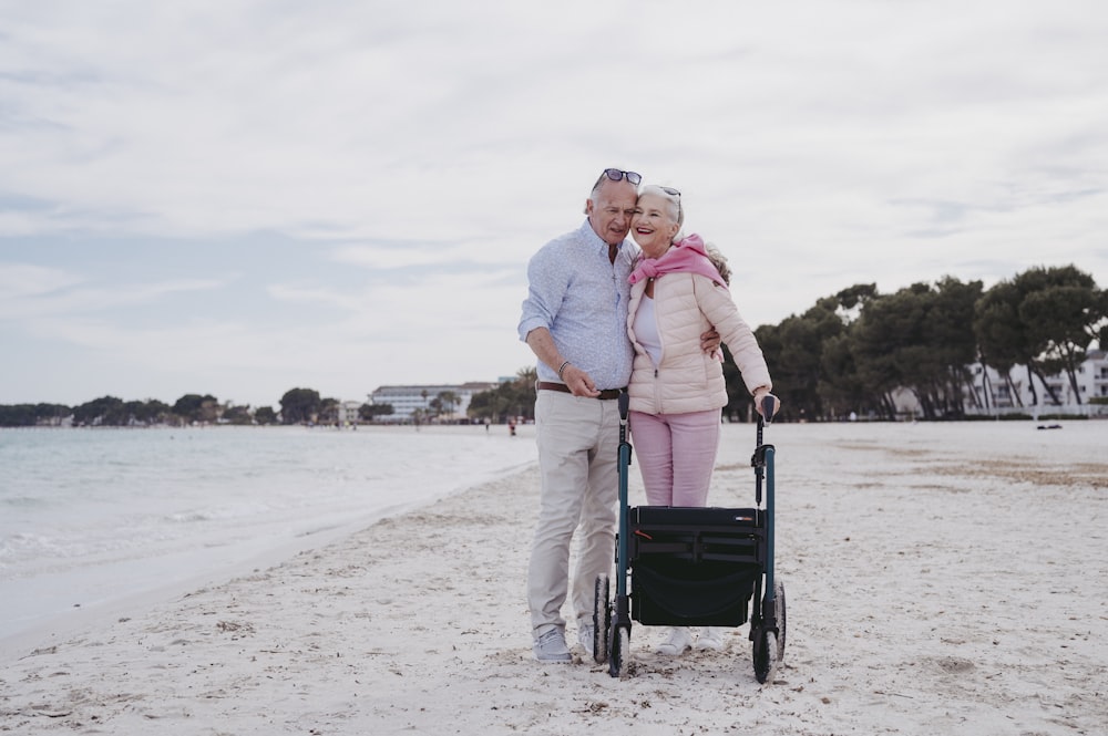 a man and woman standing on a beach with a stroller