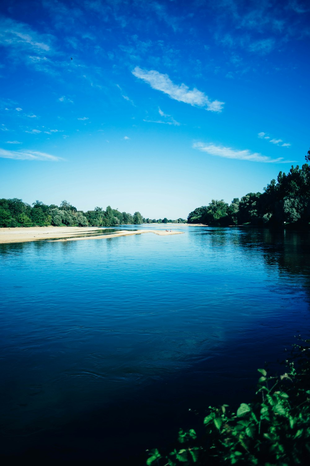 a body of water surrounded by trees under a blue sky